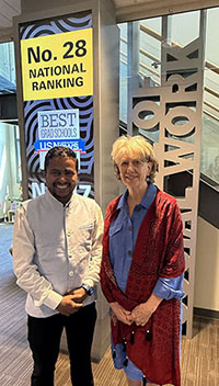 Two people stand smiling in front of a sign that says No. 28 National Ranking. Best Graduate Schools.