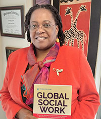 A person in a red coat and scarf holds a book that reads Global Social Work.