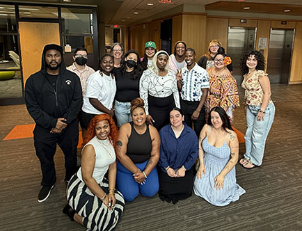 A group of 16 people stand and kneel in the lobby area of a building.